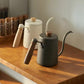 Matte black and cream-white gooseneck kettles with wood handles and lid knobs.