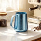 Sky-blue titanium milk pitcher with a pointed spout beside an espresso machine.