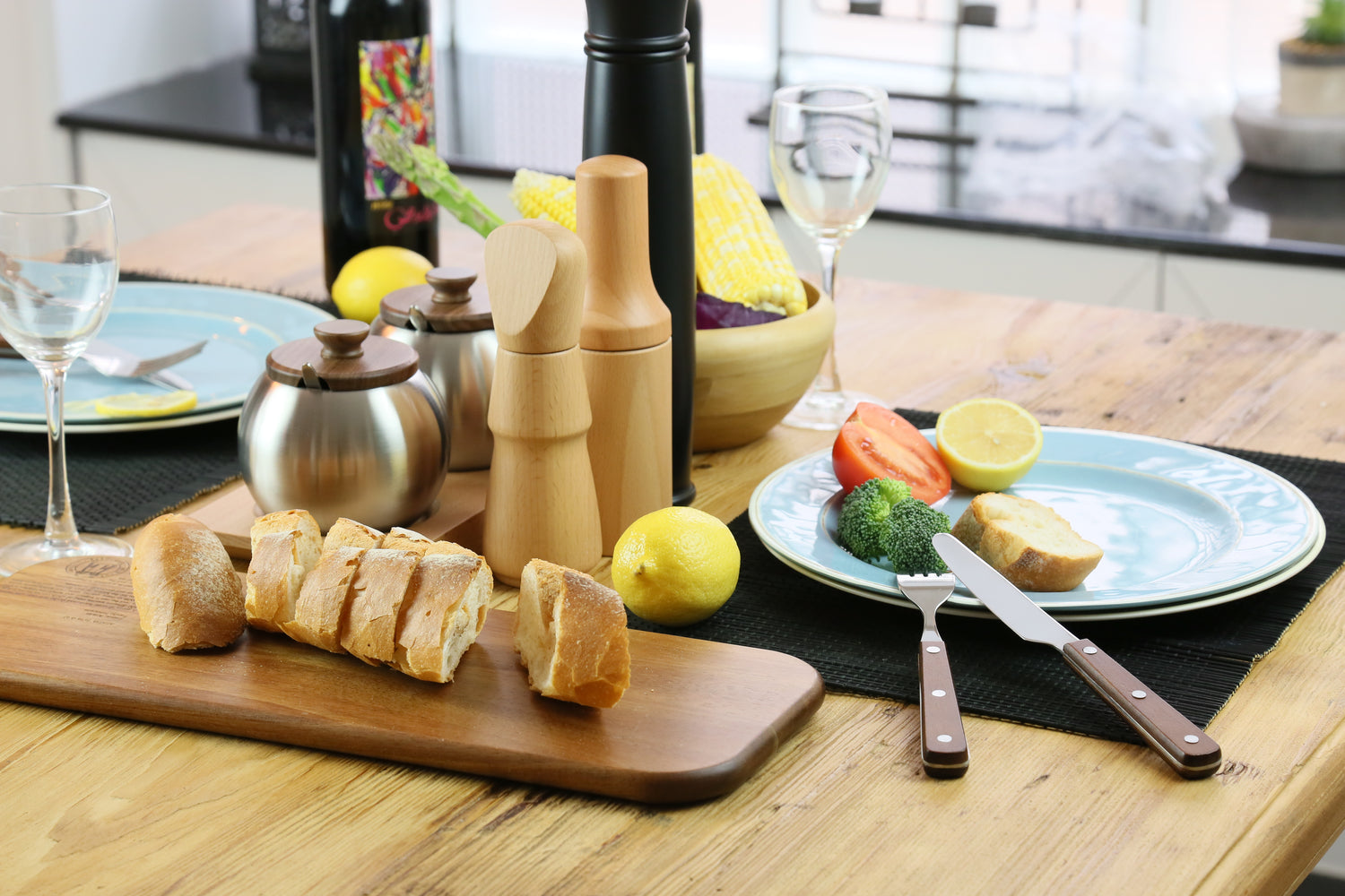 Table setting with bread, salt and pepper mills, and a plate of food in a kitchen.