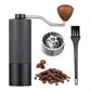 Black manual coffee grinder shown beside a burr close-up, coffee beans and a cleaning brush.