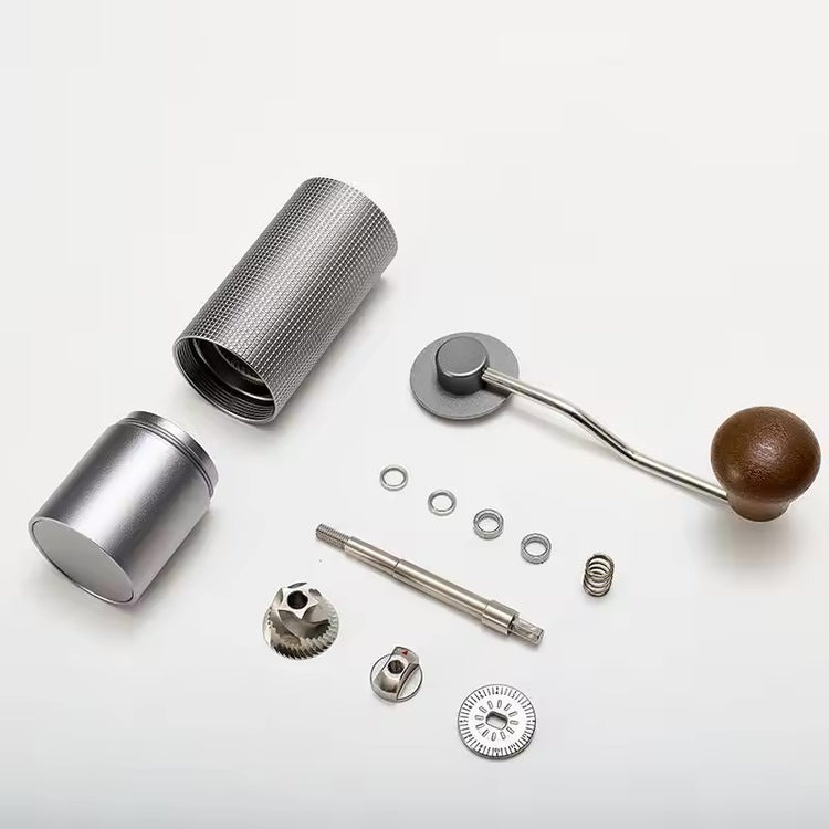 Exploded layout of a manual coffee grinder with body, shaft, bearings, burr, adjustment dial, crank and grounds cup.