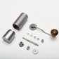Exploded layout of a manual coffee grinder with body, shaft, bearings, burr, adjustment dial, crank and grounds cup.