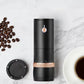 Black rechargeable electric coffee grinder beside coffee beans and a cup.