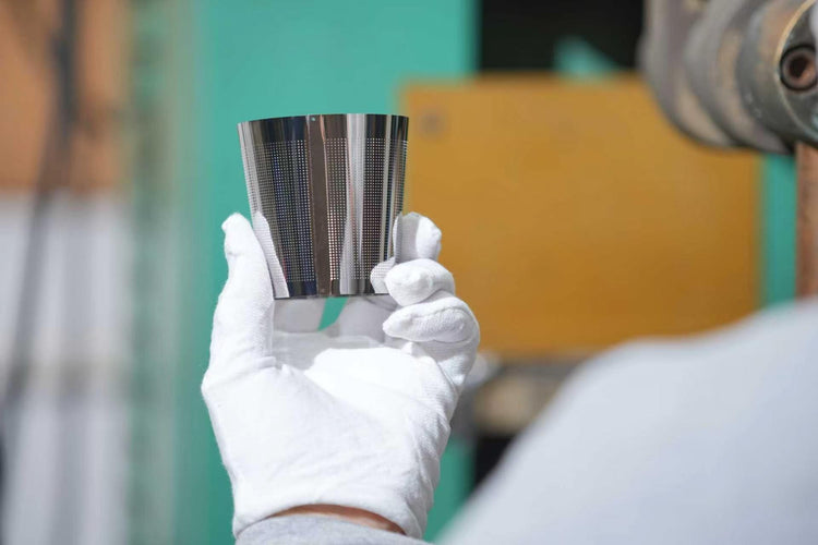 A gloved hand holding a perforated stainless-steel component